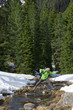 Senior man with ski poles crossing stream in snowy woods