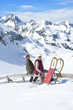 Portrait of senior couple with sled siting on fence on snowy mountain
