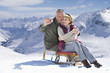 Senior couple on sled taking self-portrait with digital camera on snowy mountain