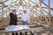 Architects with blueprints handshaking at construction site
