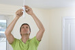 Electrician installing overhead light with compact fluorescent light bulb