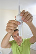 Photo: Man replacing compact fluorescent light bulb in overhead light fixture Man replacing compact fluorescent light bulb in overhead light fixture