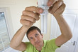 Photo: Man replacing compact fluorescent light bulb in overhead light fixture Man replacing compact fluorescent light bulb in overhead light fixture