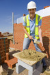 Portrait of bricklayer applying mortar to brick with trowel