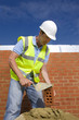Bricklayer applying mortar to brick with trowel in front of wall
