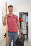 Photo: Portrait of smiling handyman with copper pipes and toolbox in front of boiler in closet Portrait of smiling handyman with copper pipes and toolbox in front of boiler in closet