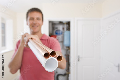 Photo: Portrait of man holding copper pipes in front of boiler in closet Portrait of man holding copper pipes in front of boiler in closet