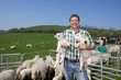 Portrait of smiling shepherd holding lambs in pasture