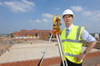 Foto: Portrait of confident surveyor with hands on hips next to theodolite at construction site Portrait of confident surveyor with hands on hips next to theodolite at construction site