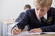 Close up of male student in school uniform taking exam at desk in classroom