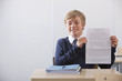 Photo: Portrait of proud student in school uniform holding graded essay at desk in classroom Portrait of proud student in school uniform holding graded essay at desk in classroom