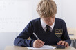 Photo: Male student in school uniform taking exam with calculator at desk in classroom Male student in school uniform taking exam with calculator at desk in classroom