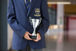 Portrait of male student in school uniform holding trophy in school corridor