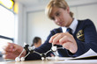 Female student in school uniform looking down at atom model on desk in classroom