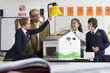 Foto: Teacher and students in school uniforms adjusting lamp over solar panels on house model in science class Teacher and students in school uniforms adjusting lamp over solar panels on house model in science class