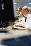 Photo: Teacher watching over students in school uniforms sitting at computers in library Teacher watching over students in school uniforms sitting at computers in library