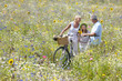Senior couple standing with bicycles in field of wildflowers with granddaughter