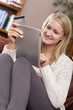 Woman sitting on sofa using credit card to shop online with digital tablet