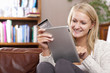 Woman sitting on sofa using credit card to shop online with digital tablet