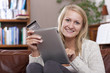 Woman sitting on sofa using credit card to shop online with digital tablet