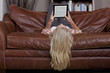 Woman laying upside-down on sofa using digital tablet
