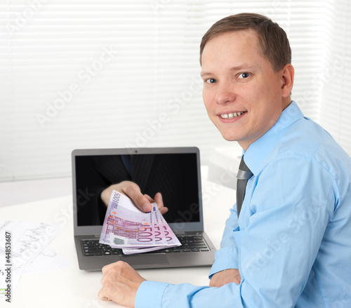 Photo: Human hand with money, coming out from the laptop computer scree Human hand with money, coming out from the laptop computer scree