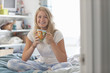 Portrait of smiling young woman in pajamas drinking coffee in bed
