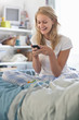 Photo: Smiling young woman in pajamas text messaging on cell phone in bed Smiling young woman in pajamas text messaging on cell phone in bed