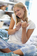 Smiling young woman in pajamas talking on cell phone and filing fingernails