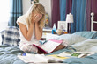 Young woman in pajamas doing homework on bed with hands covering face