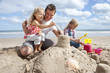 Father and daughters making sandcastle on sunny beach