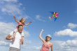 Father carrying daughter on shoulders and mother flying kite