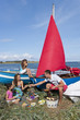Family with barbecue picnicking near boats on beach