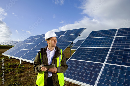 Photo: Engineer with digital tablet standing in front of solar panels Engineer with digital tablet standing in front of solar panels