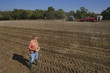 Foto: Farmer holding potatoes in sunny, rural field and watching tractors in background Farmer holding potatoes in sunny, rural field and watching tractors in background