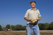 Foto: Smiling farmer holding potatoes in sunny, rural field with tractors in background Smiling farmer holding potatoes in sunny, rural field with tractors in background