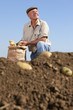 Foto: Farmer kneeling next to sack of potatoes in sunny, rural field Farmer kneeling next to sack of potatoes in sunny, rural field
