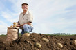 Foto: Smiling farmer kneeling next to sack of potatoes in rural field Smiling farmer kneeling next to sack of potatoes in rural field