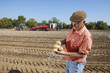 Foto: Farmer inspecting potatoes in sunny, rural field with tractors in background Farmer inspecting potatoes in sunny, rural field with tractors in background