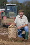 Photo: Portrait of smiling farmer with sack of potatoes in sunny, rural field with tractor in background Portrait of smiling farmer with sack of potatoes in sunny, rural field with tractor in background