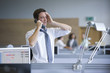 Businessman talking on telephone with head in hands in office