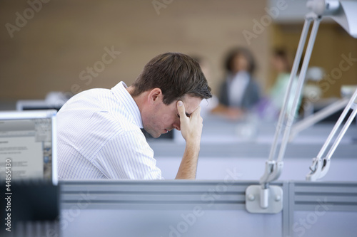 Photo: Businessman looking down with head in hands in office Businessman looking down with head in hands in office