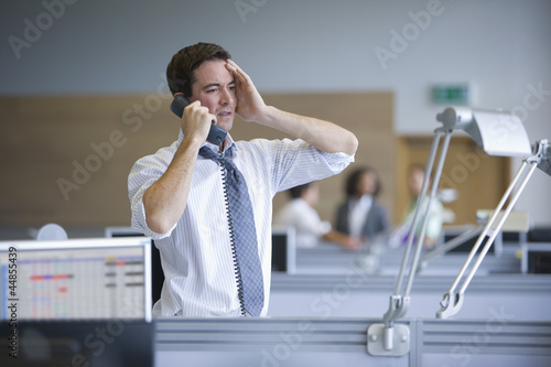 Photo: Businessman talking on telephone with head in hands in office Businessman talking on telephone with head in hands in office