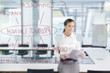 Businesswoman with paperwork looking at flow chart on glass window
