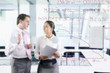 Photo: Businessman and businesswoman talking in conference room with graph on glass window in foreground Businessman and businesswoman talking in conference room with graph on glass window in foreground