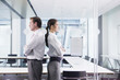 Businessman and businesswoman standing back to back in conference room