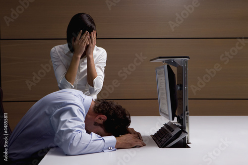 Photo: Exhausted businessman and businesswoman at desk in office Exhausted businessman and businesswoman at desk in office