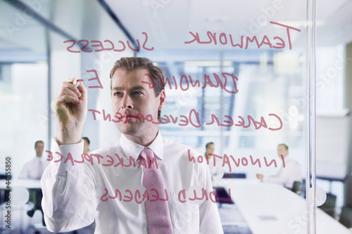 Photo: Businessman writing on glass window in office Businessman writing on glass window in office