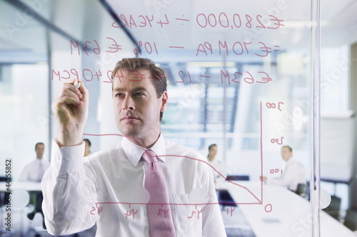 Photo: Businessman drawing graph on glass window in office Businessman drawing graph on glass window in office