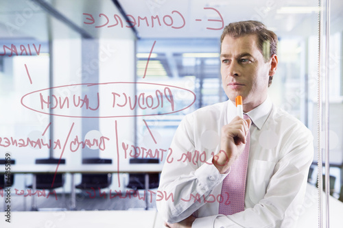 Photo: Businessman looking at flow chart on glass window Businessman looking at flow chart on glass window
